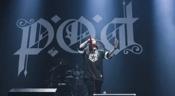 Sonny Sandoval z P.O.D. śpiewa na scenie, z charakterystycznym logo zespołu w tle.