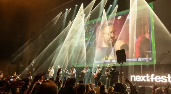 Zespół na scenie podczas koncertu na Next Fest. W tle wielki ekran z transmisją i światła.