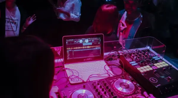 DJ Glasse miksuje muzykę na imprezie. Laptop i sprzęt DJ-ski w różowym świetle.