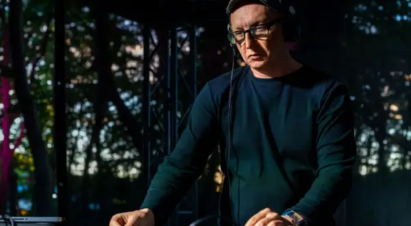 Mr Lex w okularach i czapce, w słuchawkach, miksuje muzykę na konsoli DJ-skiej.