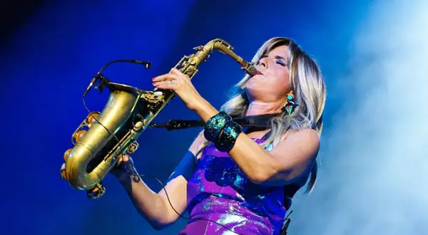 Candy Dulfer gra na saksofonie, jej blond włosy opadają na fioletową, błyszczącą sukienkę.