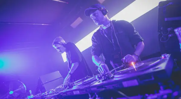 Dwóch techno djs w słuchawkach miksuje muzykę na żywo, tworząc energetyczną atmosferę na scenie.