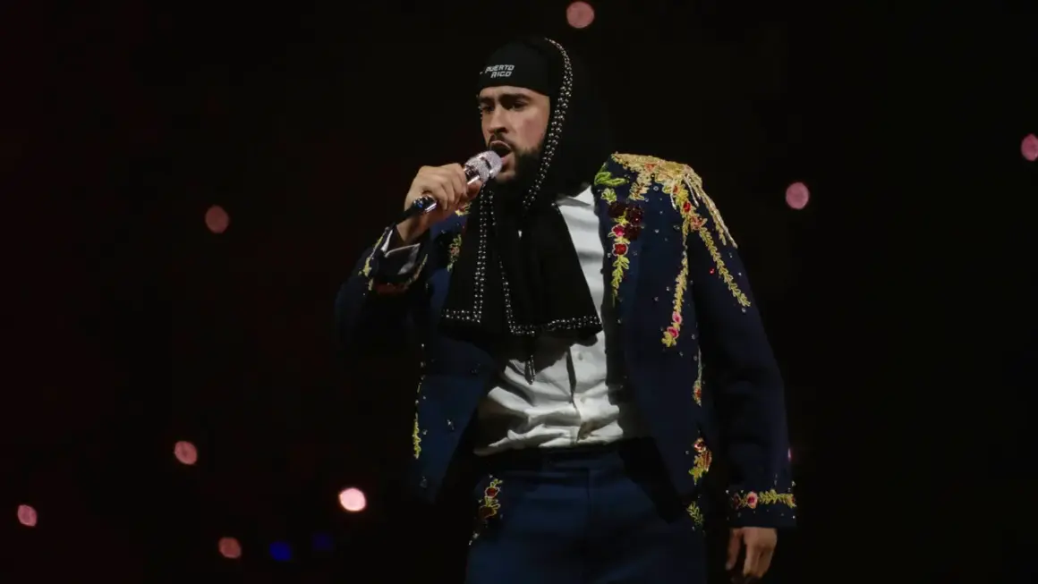 Bad Bunny w Polsce, w ozdobnej marynarce i czapce z napisem "Puerto Rico", śpiewa do mikrofonu na tle rozmytych świateł.