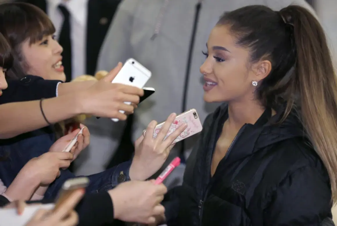 Ariana Grande w Polsce, otoczona fanami z telefonami, którzy chcą zrobić jej zdjęcie.
