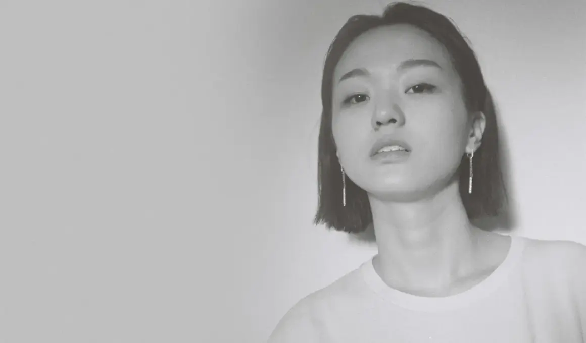 Park Hye Jin, młoda kobieta o krótkich włosach i delikatnym spojrzeniu, w białej koszulce i długich kolczykach.