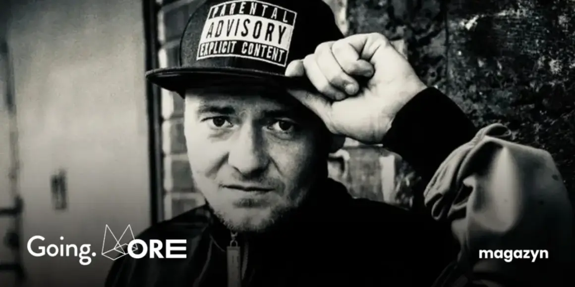 Mężczyzna w czapce z napisem "Parental Advisory Explicit Content" poprawia ją ręką. Jego spojrzenie jest intensywne, jakby mówił: "joka kaliber".