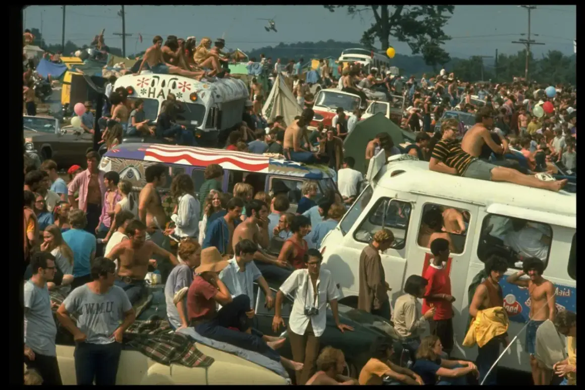 Tłum ludzi na festiwalu, siedzący na dachach vanów i samochodów. To właśnie woodstock co to za wydarzenie?