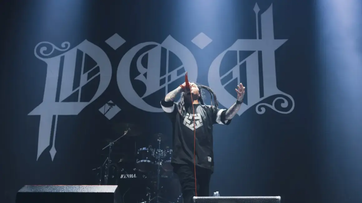 Sonny Sandoval z P.O.D. śpiewa na scenie, z charakterystycznym logo zespołu w tle.