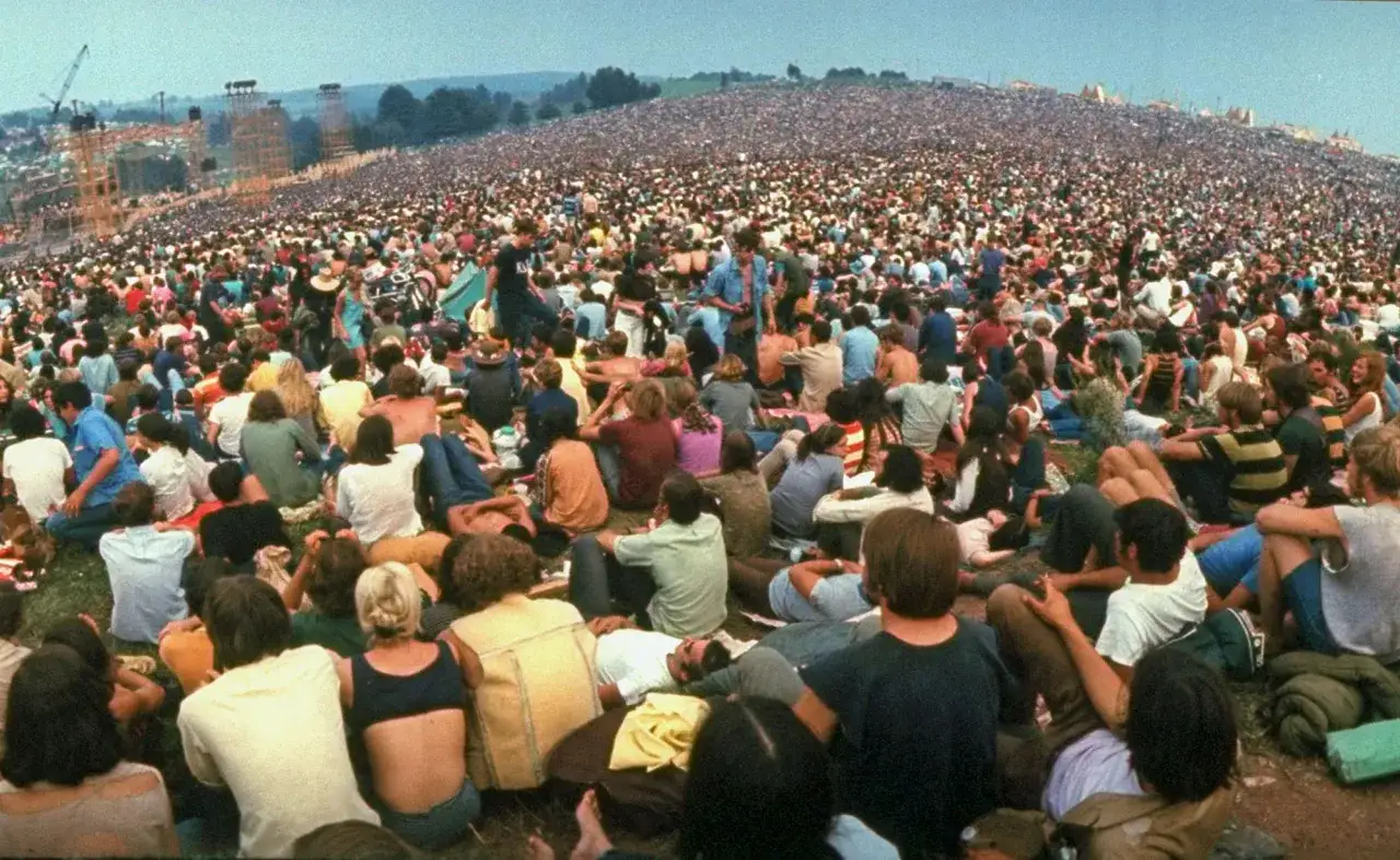 Tłum ludzi na festiwalu Woodstock. To właśnie woodstock co to za wydarzenie? Ogromna scena i tysiące uczestników.