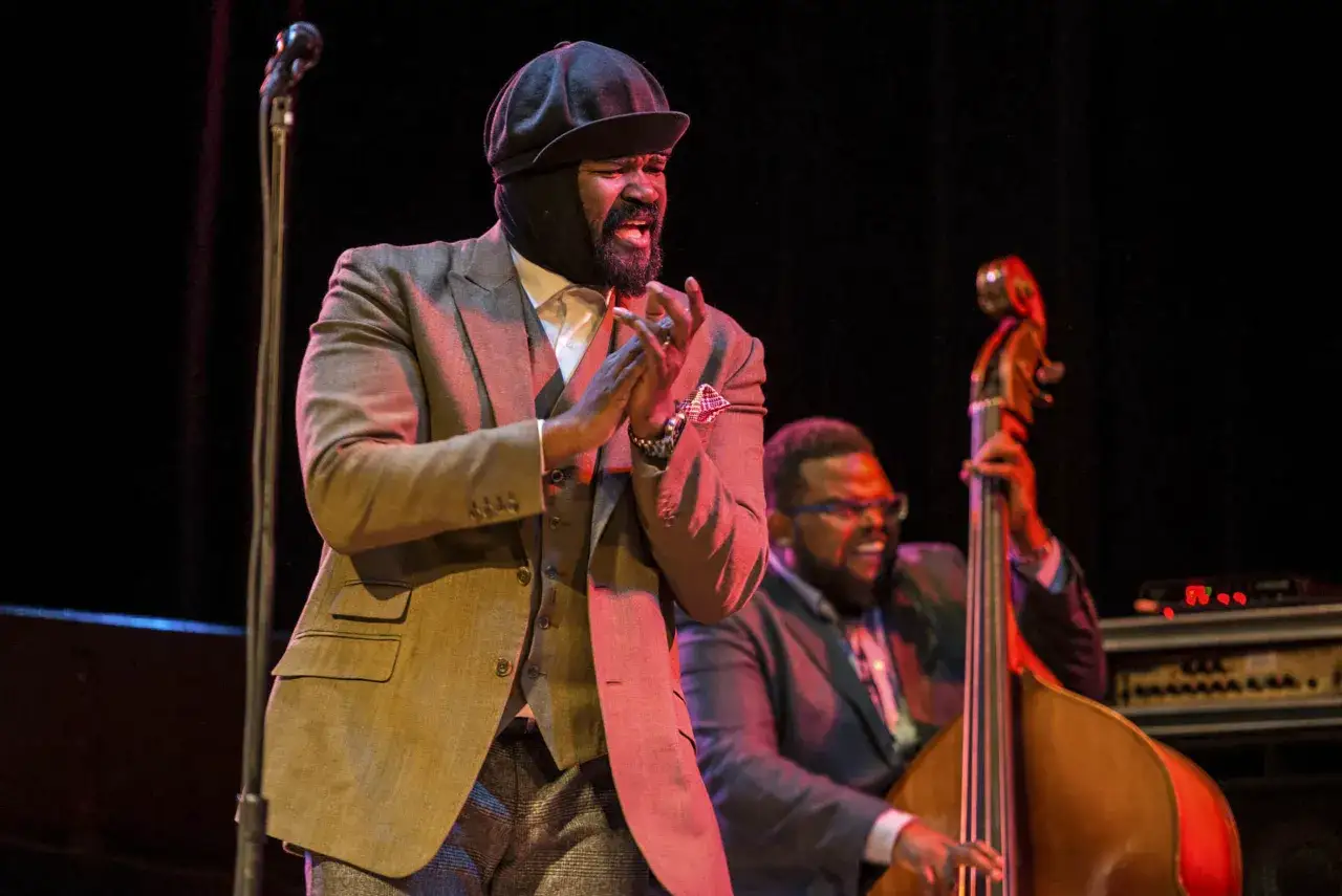 Gregory Porter w kapeluszu i garniturze śpiewa na scenie, obok kontrabasista.