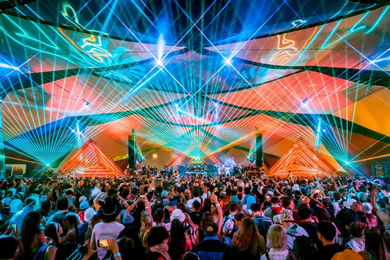 Tłum ludzi na rave festivalu pod laserami i kolorowymi światłami.