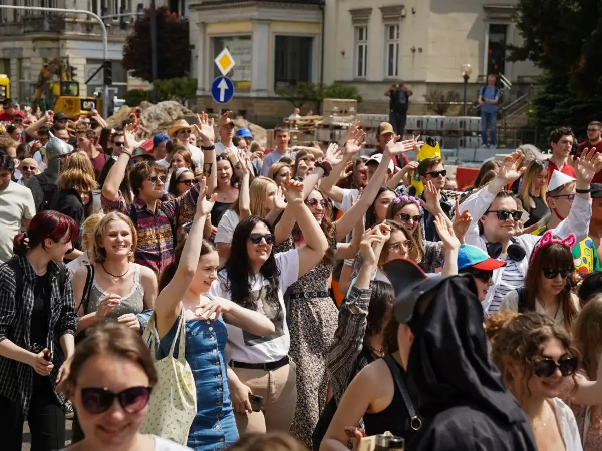 Tłum młodych ludzi na ulicy, machają rękami. To z pewnością juwenalia, czyli święto studentów.