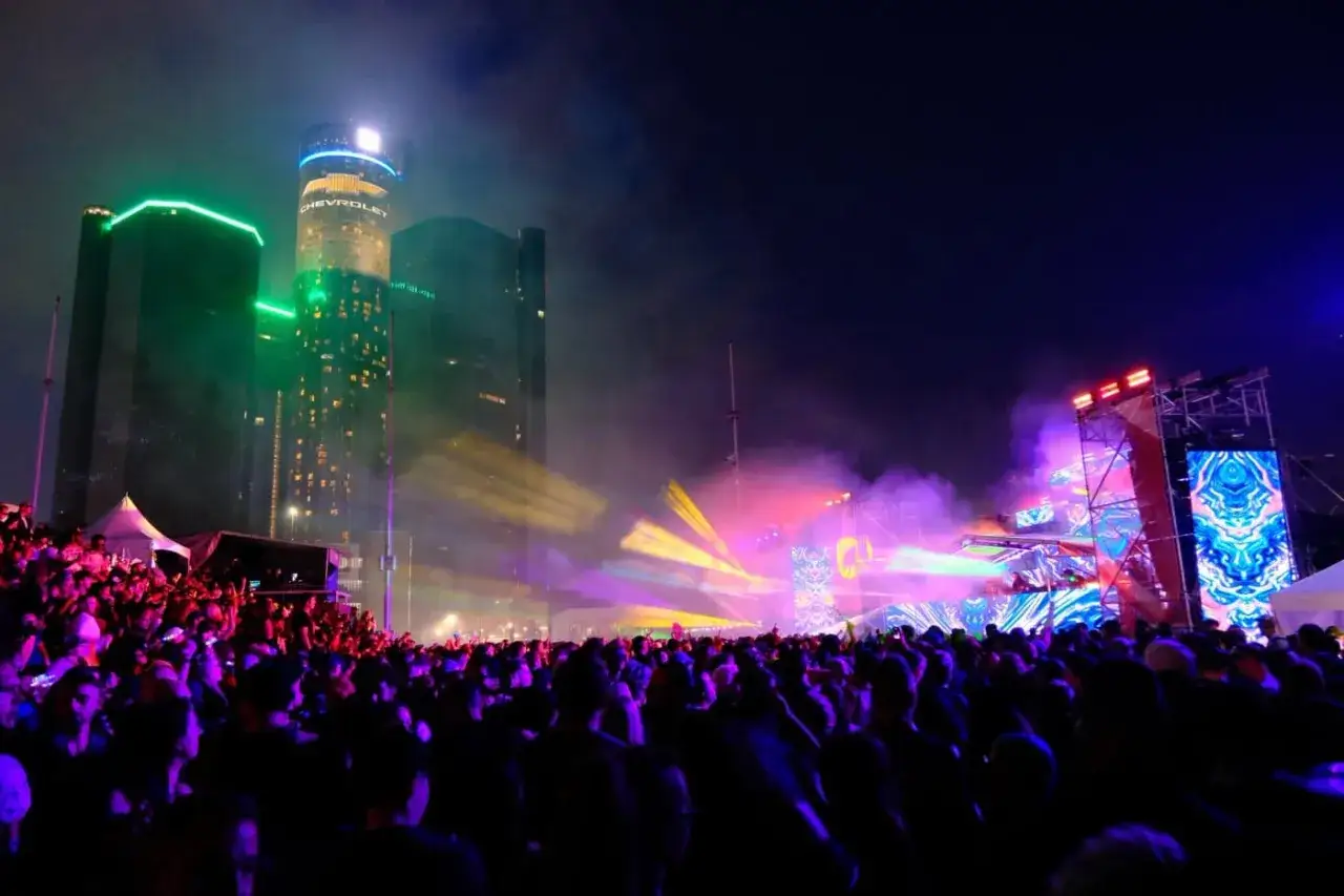 Tłum ludzi na nocnym festiwalu techno pod oświetlonymi wieżowcami. To jedna z największych imprez techno na świecie.
