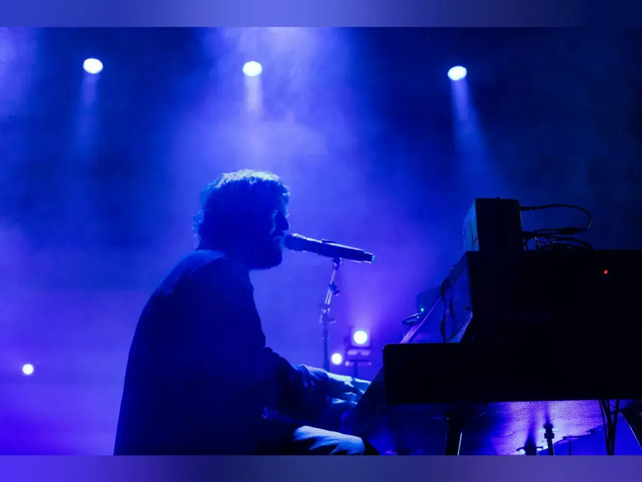 Chet Faker, w blasku niebieskich świateł, gra na keyboardzie i śpiewa do mikrofonu.