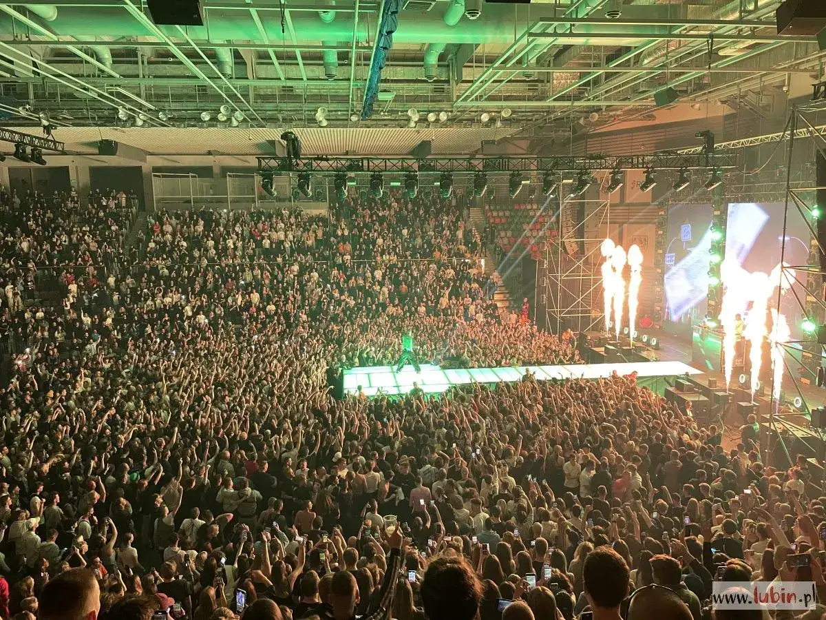 Oki raper na scenie, tłum szaleje, płomienie buchają. Koncert w hali pełnej fanów.