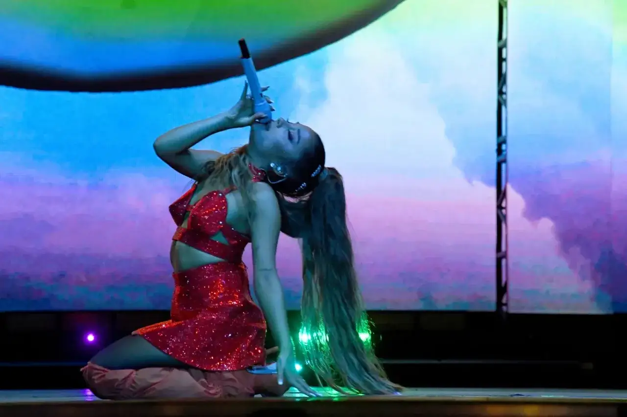 Ariana Grande w błyszczącej czerwonej kreacji na scenie, śpiewająca do mikrofonu. Polska publiczność szaleje!