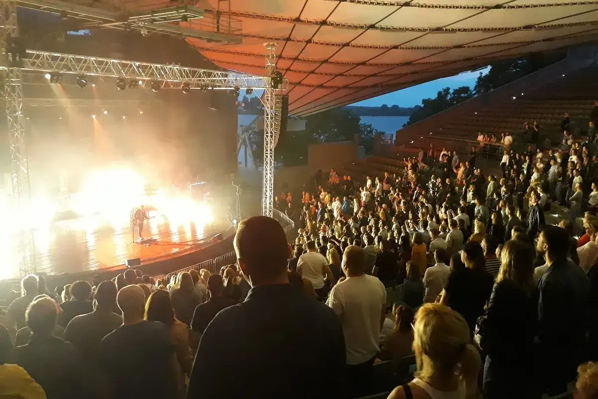 Krzysztof Zalewski koncert na żywo. Tłum widzów w amfiteatrze, artysta na scenie oświetlonej jaskrawymi światłami.