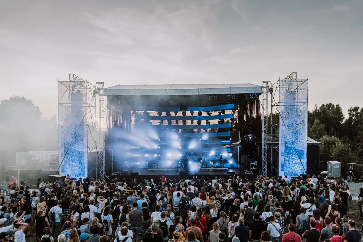 Tłumy ludzi na koncercie podczas jastarnia festiwal. Na scenie gra zesp&oacute;ł, a nad publicznością unosi się mgła i światła.