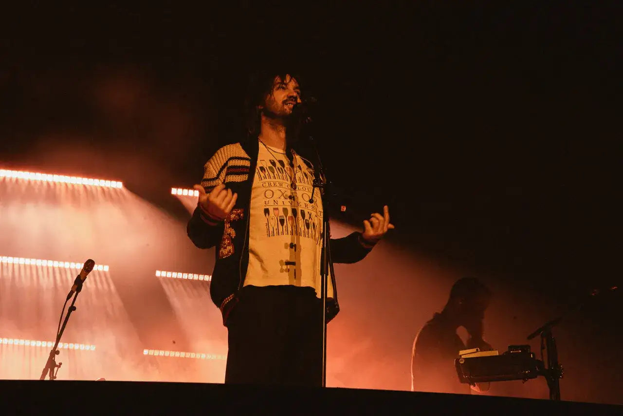 Kevin Parker z Tame Impala Polska na scenie, w świetle reflektorów, z mikrofonem.