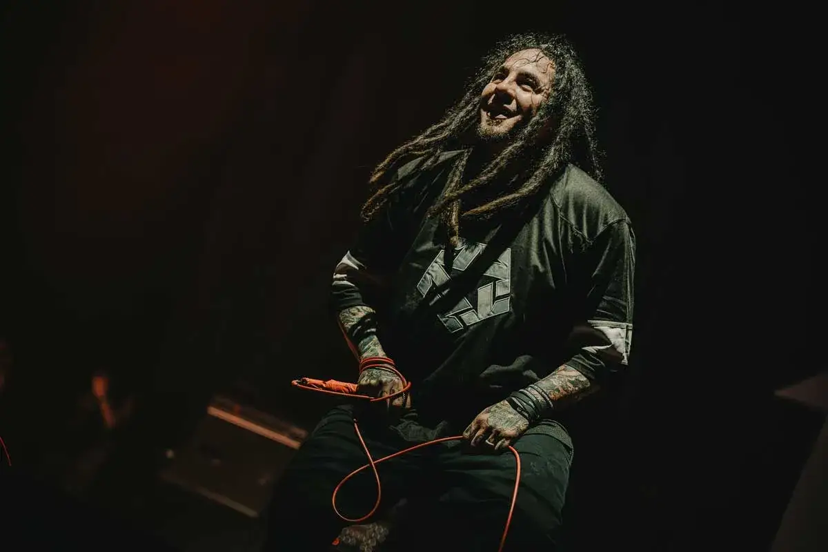 Sonny Sandoval, wokalista z dredami, śpiewa z pasją na scenie, trzymając mikrofon.