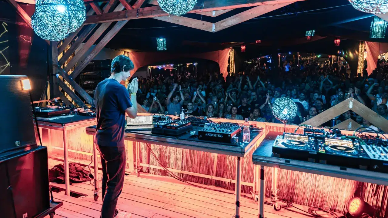 DJ Mauro Picotto gra dla roztańczonego tłumu pod wiszącymi lampami.