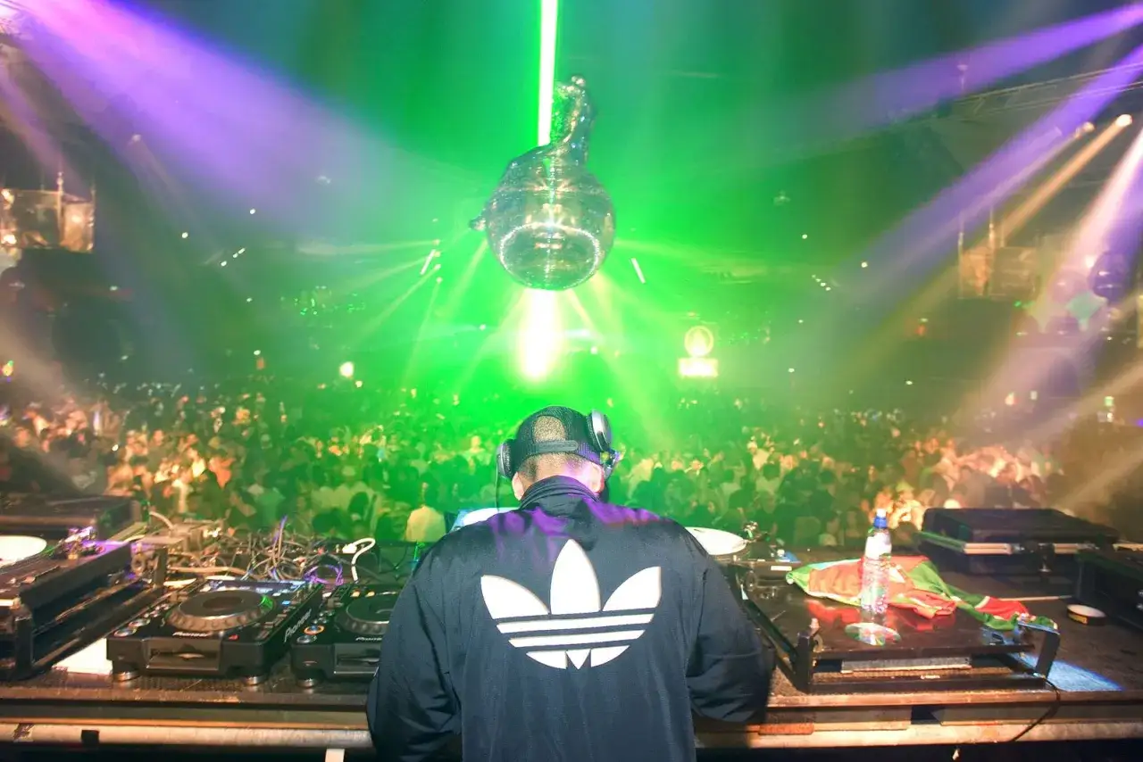 DJ w klubie, tłum szaleje przy muzyce techno lata 2000. Wykonawcy tworzą niezapomnianą atmosferę.