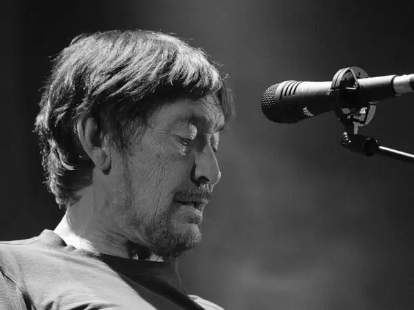 Chris Rea, zamyślony, przed mikrofonem na scenie.