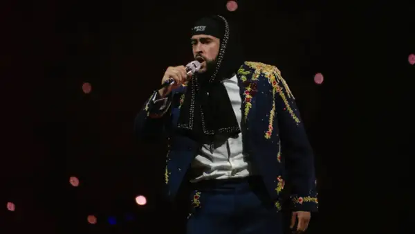 Bad Bunny w Polsce, w ozdobnej marynarce i czapce z napisem "Puerto Rico", śpiewa do mikrofonu na tle rozmytych świateł.