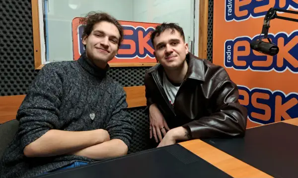 Dwóch młodych mężczyzn w studiu radiowym. Jeden w swetrze, drugi w skórzanej kurtce. Może to jeżyk raper i jego kolega?