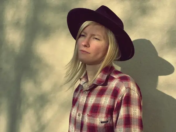 Agata Karczewska, jak "dark horse", w kapeluszu i kratowanej koszuli, spogląda w bok. Cień rzuca się na ścianę.