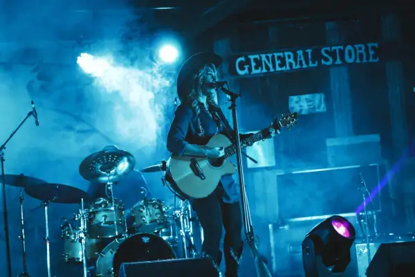 Gwiazdy country w kowbojskich kapeluszach grają na gitarach i śpiewają na scenie, otoczone dymem i niebieskim światłem.