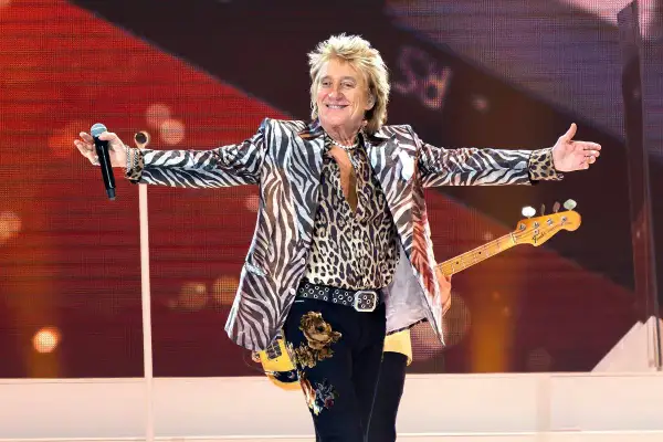 Rod Stewart w panterce i marynarce w zebrę, z gitarą basową, na scenie, jakby to był największy koncert na świecie.