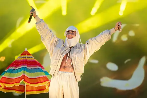 Artysta w białej stylizacji, z mikrofonem w dłoni, na tle kolorowego parasola i żółtych świateł. To musi być koncert SBM!