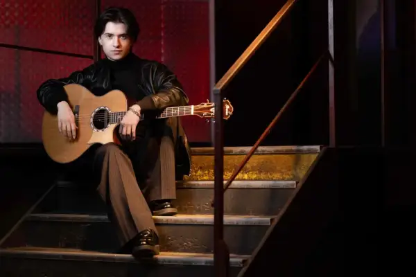 Marcin Patrzałek na koncercie, siedząc na schodach z gitarą, gotowy do występu.