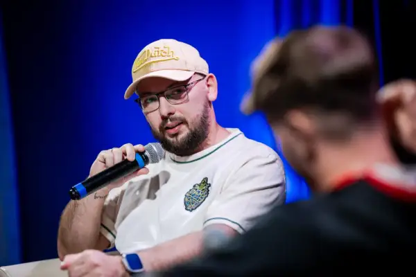 Raper Edzio w bejsbolówce Von Dutch i okularach, trzymający mikrofon, podczas panelu dyskusyjnego.
