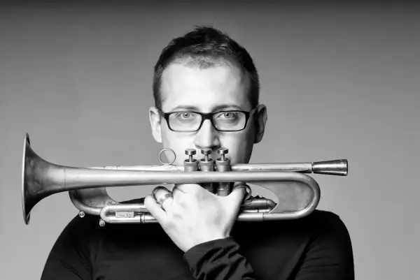 Maciej Fortuna, muzyk z trąbką, w okularach, zamyślony.