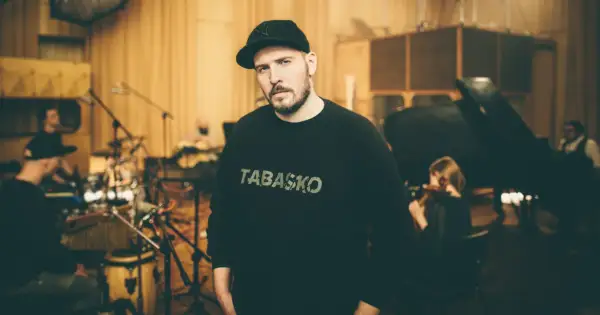 W studiu nagraniowym, w otoczeniu muzyków, stoi jeden z legend polskiego rapu, w bluzie z napisem "TABASKO".