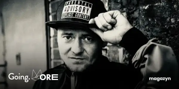 Mężczyzna w czapce z napisem "Parental Advisory Explicit Content" poprawia ją ręką. Jego spojrzenie jest intensywne, jakby mówił: "joka kaliber".
