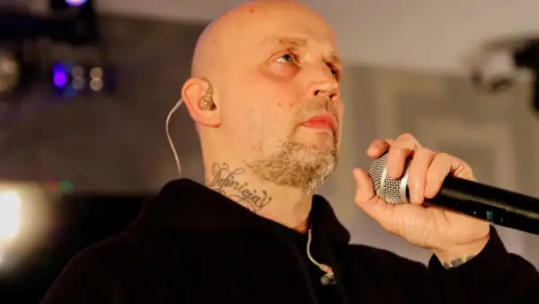 Peja z mikrofonem, w tle światła sceniczne. DJ decki czekają na jego wejście.