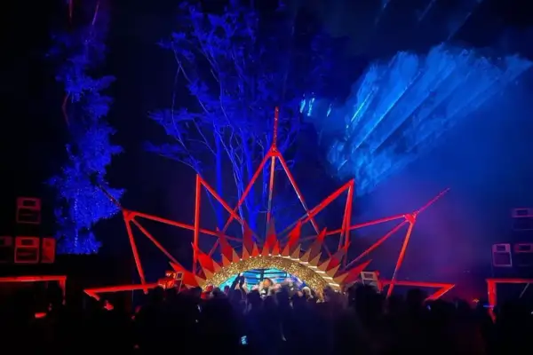 Nocny rave festival z laserami i sceną w kształcie korony. Tłum bawi się w rytm muzyki.