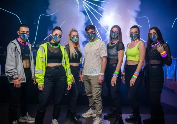 Grupa młodych ludzi w maskach i neonowych akcesoriach, gotowa na energetyczny koncert techno.