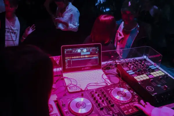 DJ Glasse miksuje muzykę na imprezie. Laptop i sprzęt DJ-ski w różowym świetle.