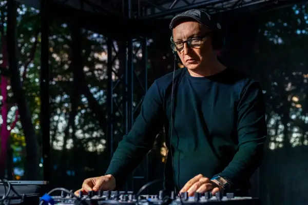 Mr Lex w okularach i czapce, w słuchawkach, miksuje muzykę na konsoli DJ-skiej.