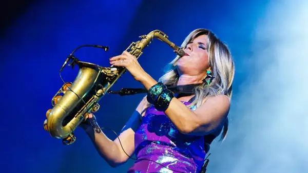 Candy Dulfer gra na saksofonie, jej blond włosy opadają na fioletową, błyszczącą sukienkę.