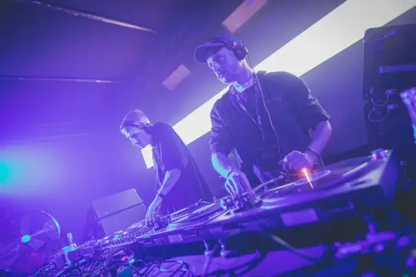 Dwóch techno djs w słuchawkach miksuje muzykę na żywo, tworząc energetyczną atmosferę na scenie.